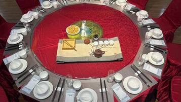 A round table set for a meal with a red tablecloth, surrounded by red chairs.