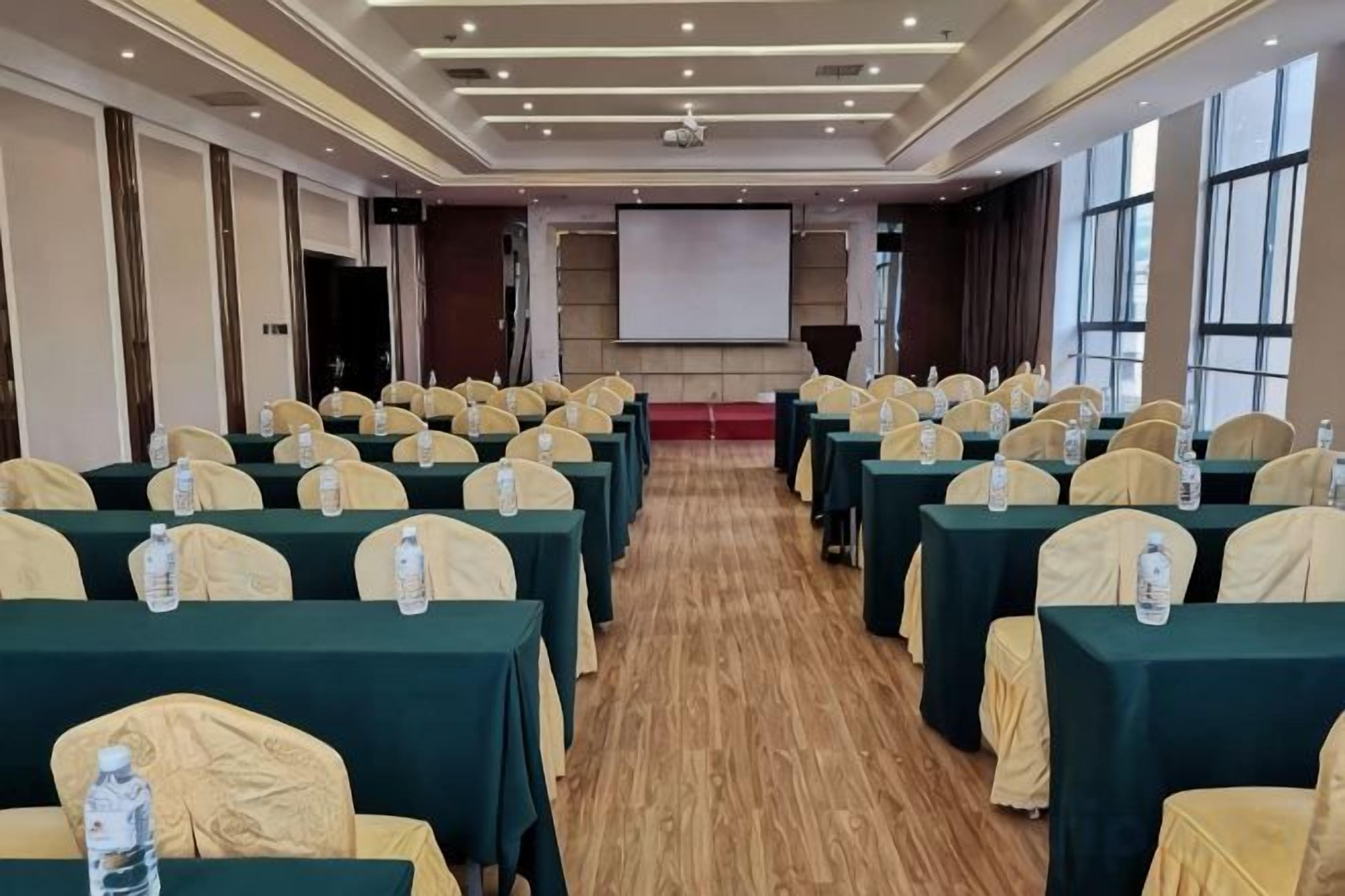 A conference room with rows of tables, chairs, and a projector screen.