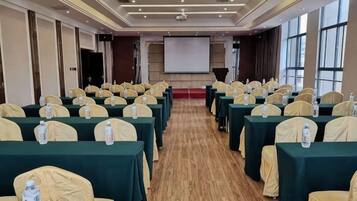 A conference room with rows of tables, chairs, and a projector screen.