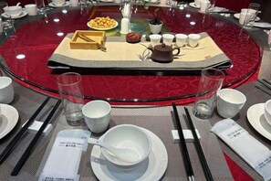 A round table with a red tablecloth, a tray with tea utensils, and a teapot.