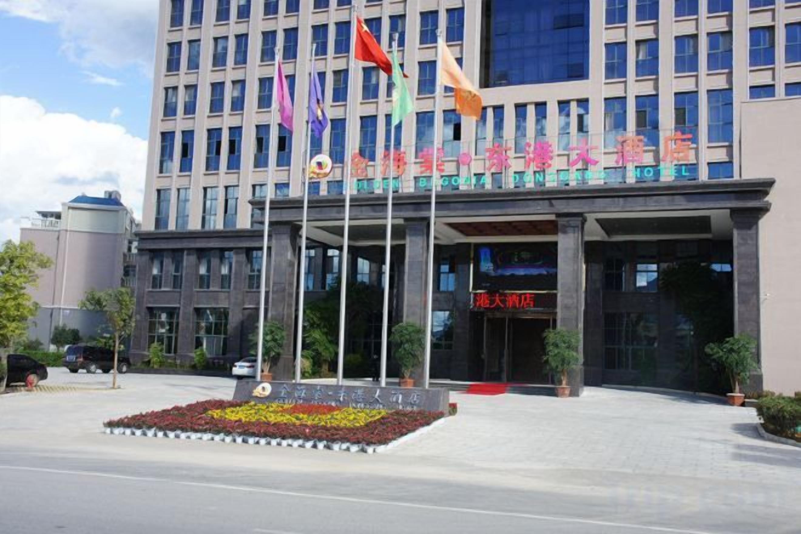 A hotel entrance with multiple flags, a large entrance canopy, and a flower bed in the foreground.