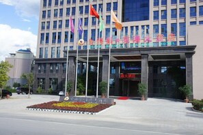 A hotel entrance with multiple flags, a large entrance canopy, and a flower bed in the foreground.