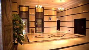 A spacious lobby with a geometric floor design, a large potted plant, and a modern chandelier. - Golden Begonia Donggang Hotel Lincang (Lincang)