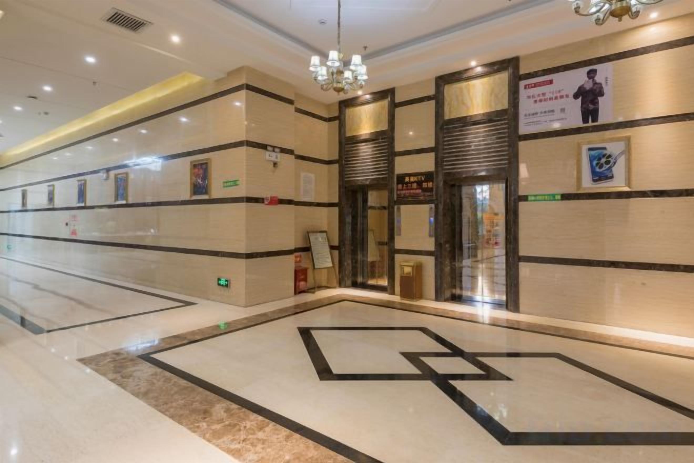 A hotel lobby with a geometric floor design, a chandelier, and a reception area with a sign.