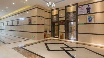 A hotel lobby with a geometric floor design, a chandelier, and a reception area with a sign.