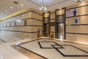 A hotel lobby with a geometric floor design, a chandelier, and a reception area with a sign.