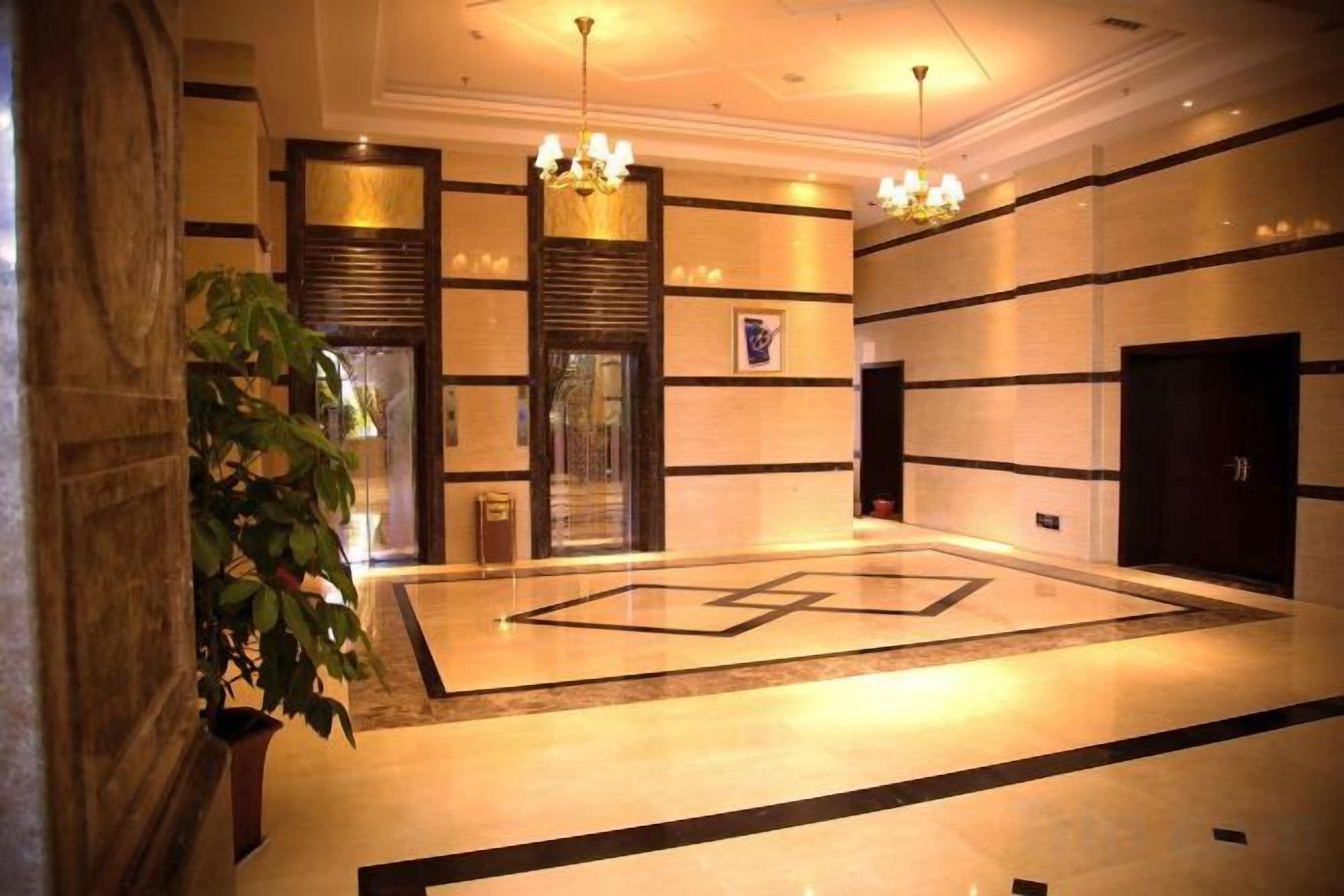 A lobby with a geometric floor design, a large potted plant, and a chandelier.