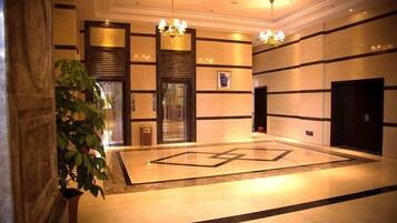 A lobby with a geometric floor design, a large potted plant, and a chandelier.