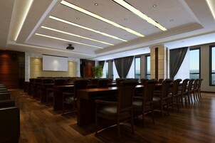 Un salón de conferencias con una larga mesa, sillas, una pantalla de proyector y un amplio ventanal.