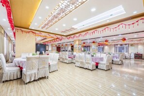 Uma sala de banquetes com várias mesas redondas, cada uma rodeada por cadeiras brancas.