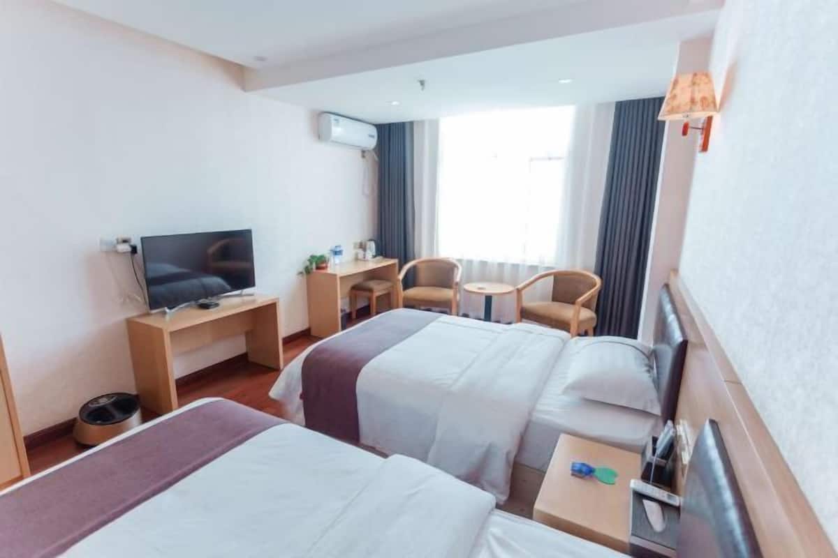 Hotelkamer met twee bedden, een bureau, een stoel, een televisie en een raam met gordijnen.