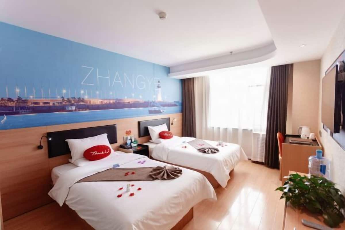 Een hotelkamer met twee bedden, een muurschildering van een stadsgezicht, een flatscreen televisie en een plant.