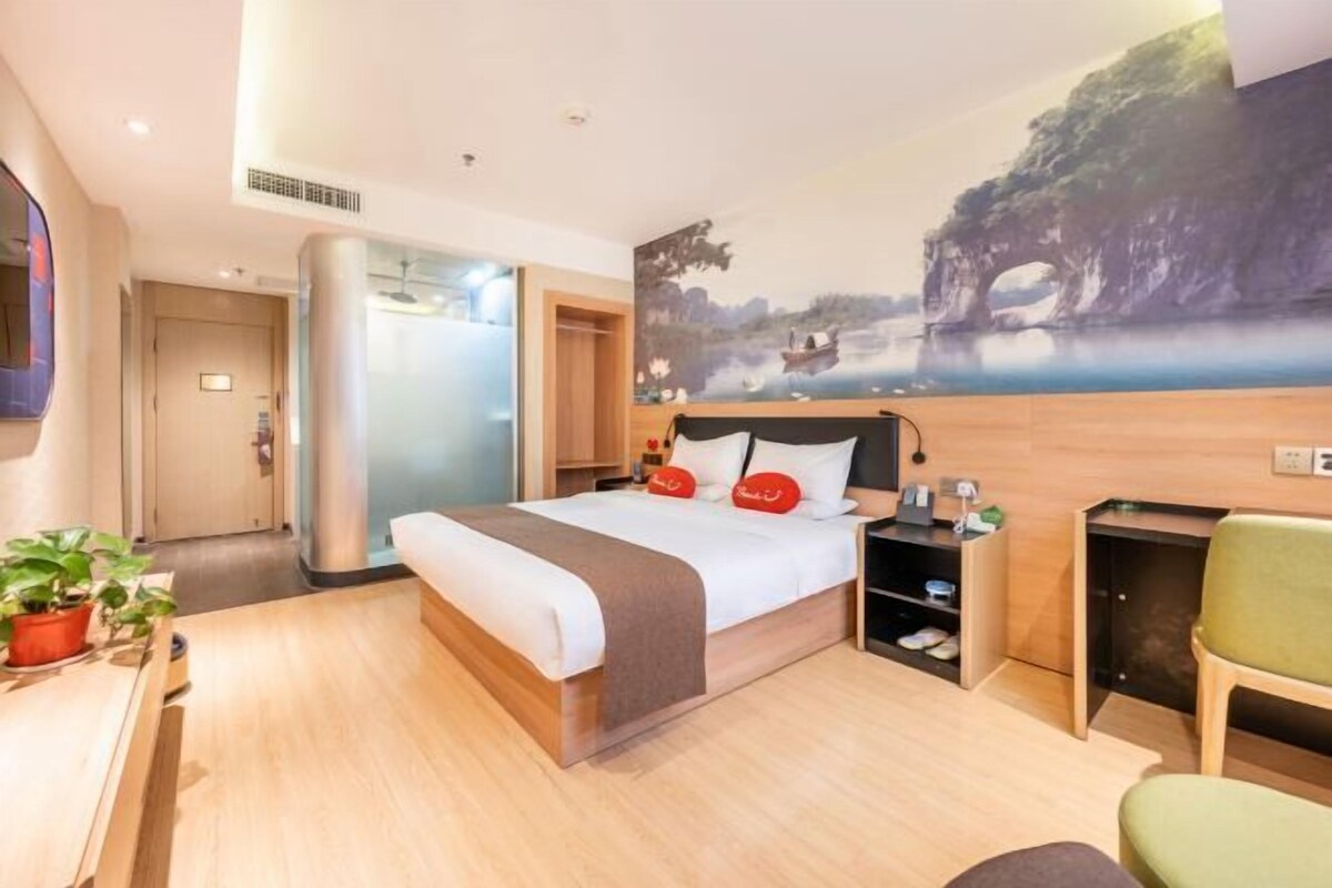 Ein modernes Hotelzimmer mit einem großen Bett, einem Schreibtisch, einem Stuhl und einem Landschaftsbild an der Wand.