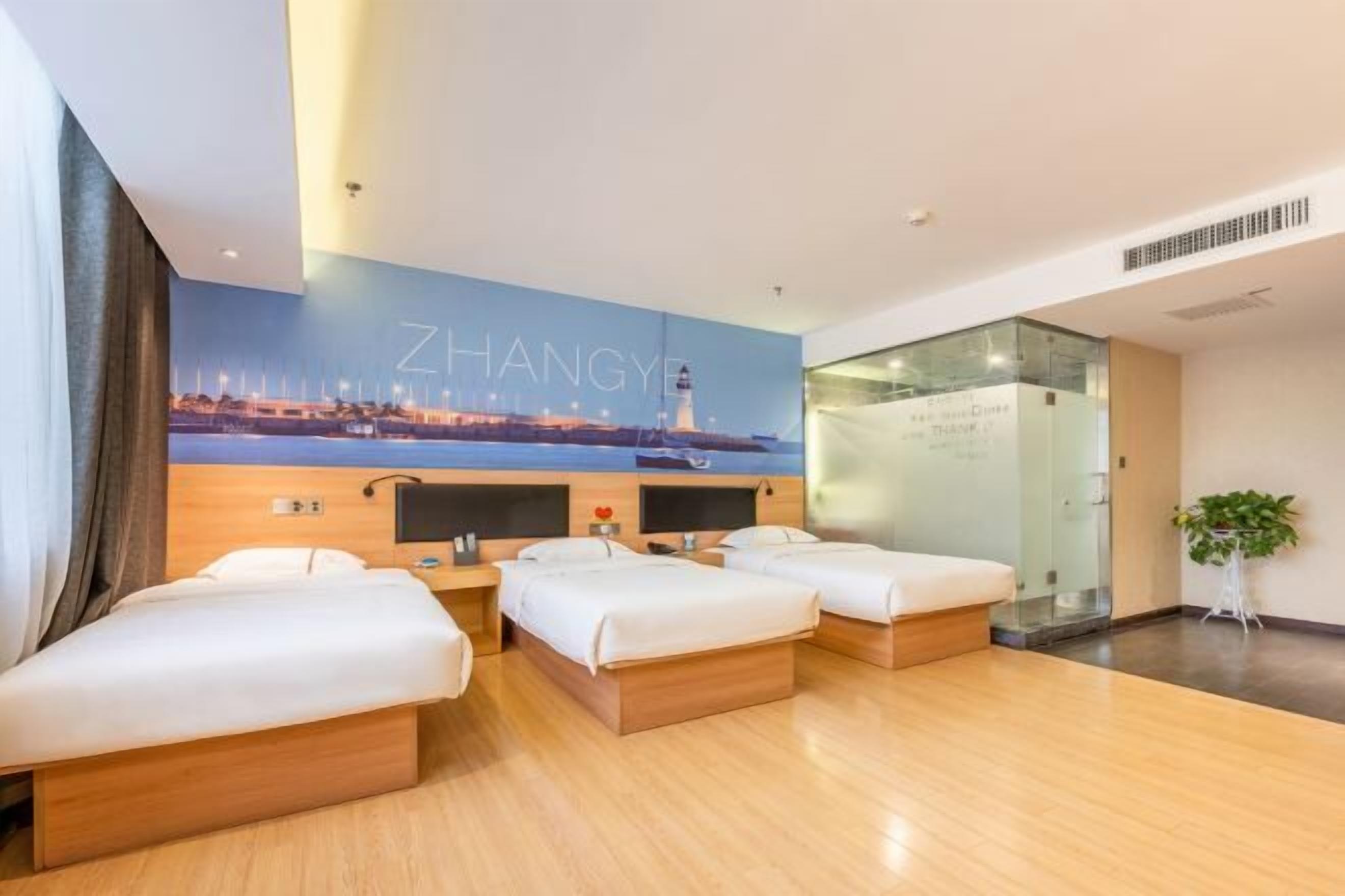 Quarto de hotel com quatro camas, um mural da paisagem urbana, uma divisória de vidro e uma planta.