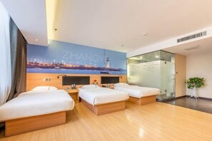 Ein Hotelzimmer mit vier Betten, einem Stadtbild-Wandgemälde, einer Glastrennwand und einer Pflanze.