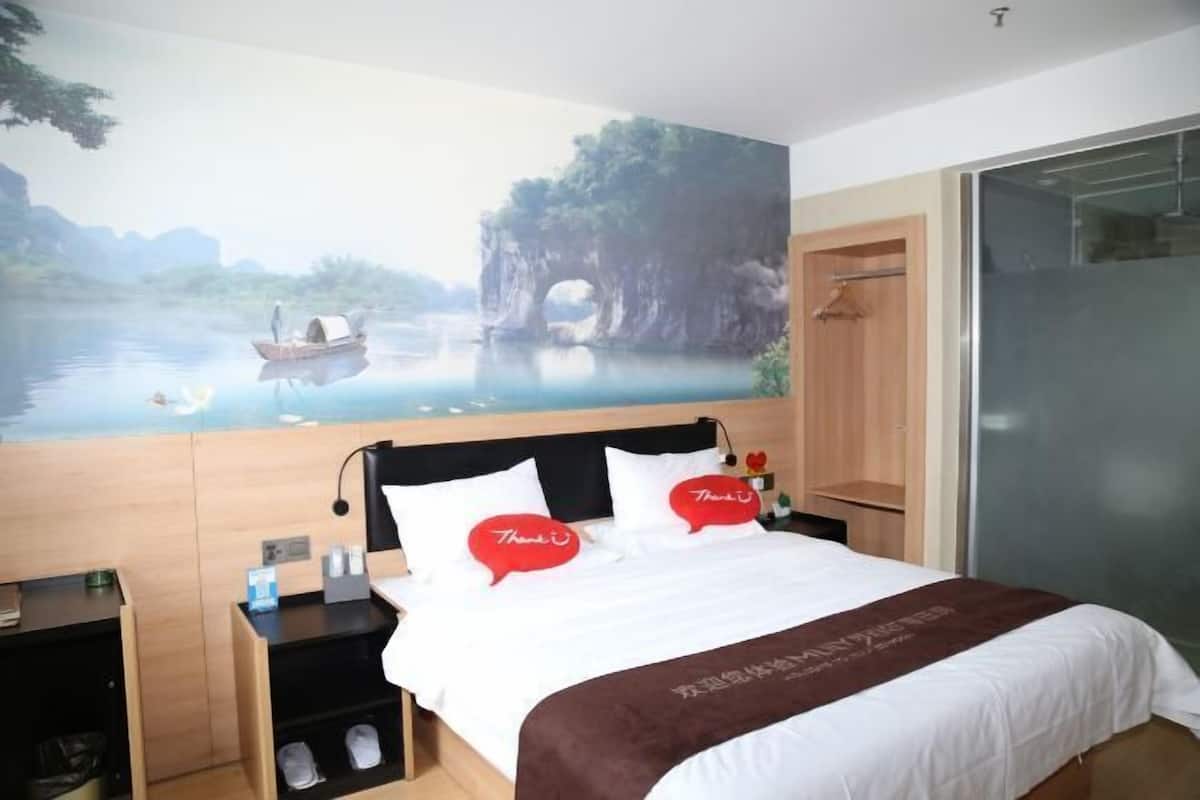 Een hotelkamer met een bed, nachtkastje, houten kledingkast en een groot raam.