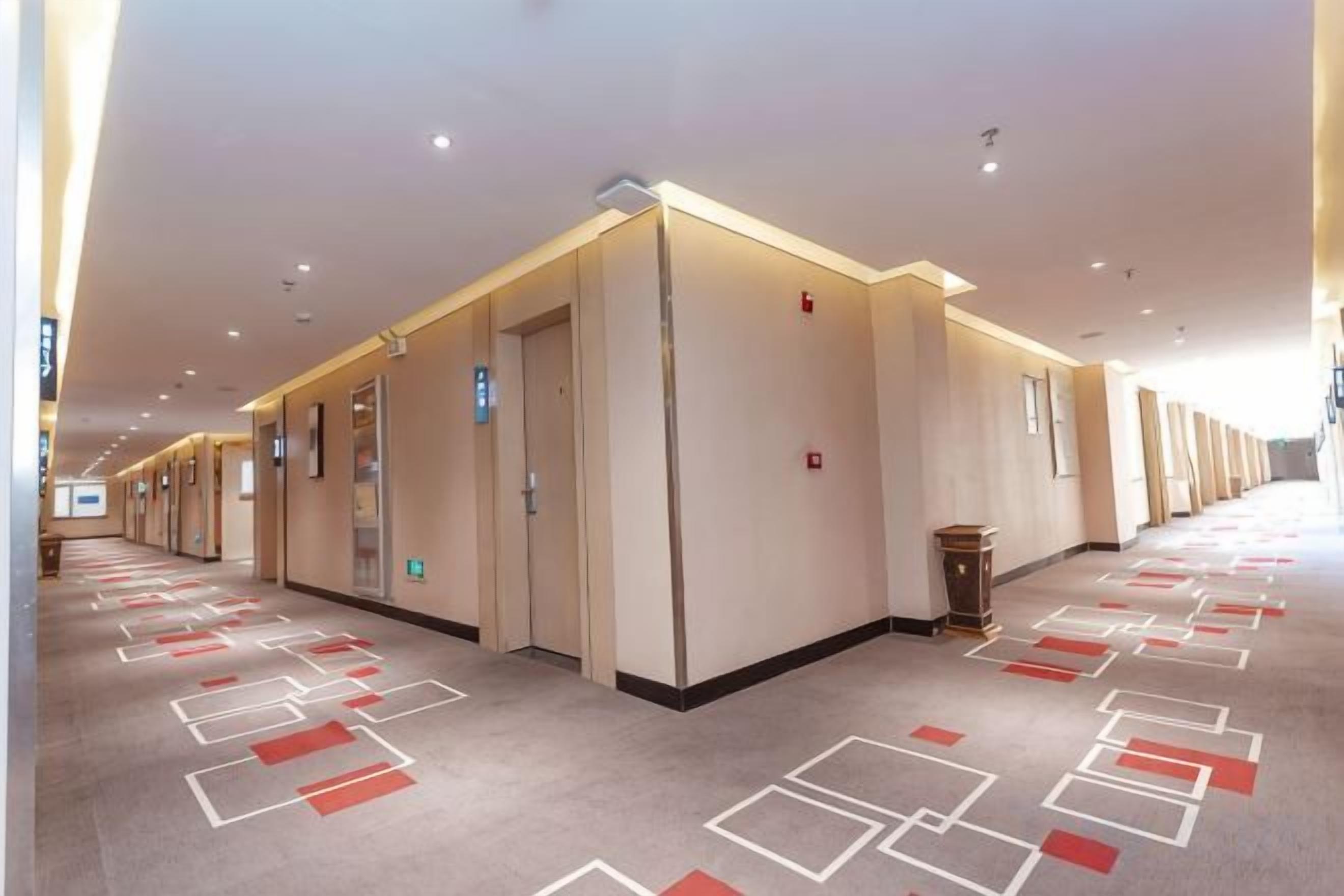 Un couloir d’hôtel avec de nombreuses portes, chacune portant une plaque indiquant le numéro de la chambre, et un tapis à motifs.