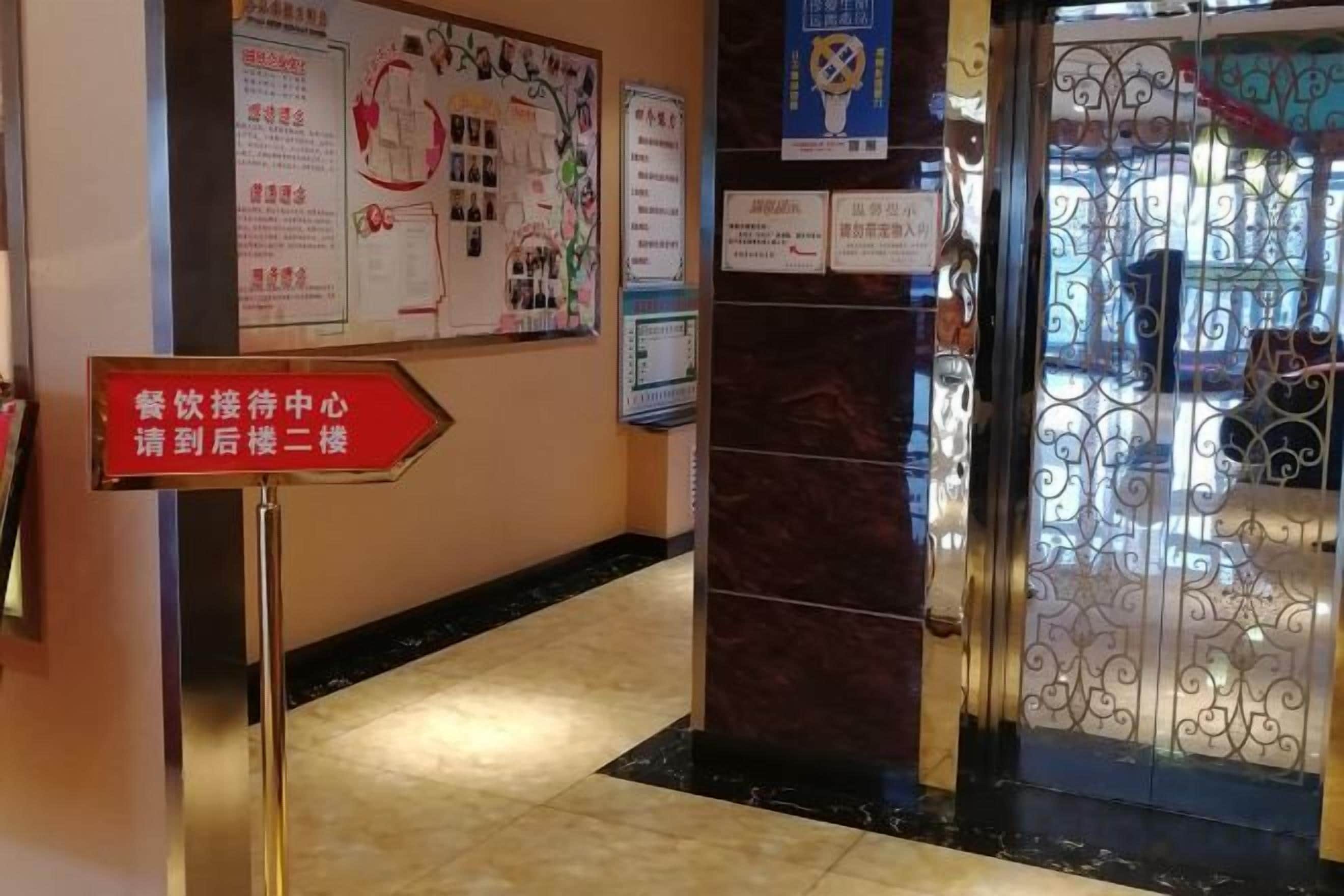 Een hotellobby met een receptiebalie, informatieposters en een routebord.