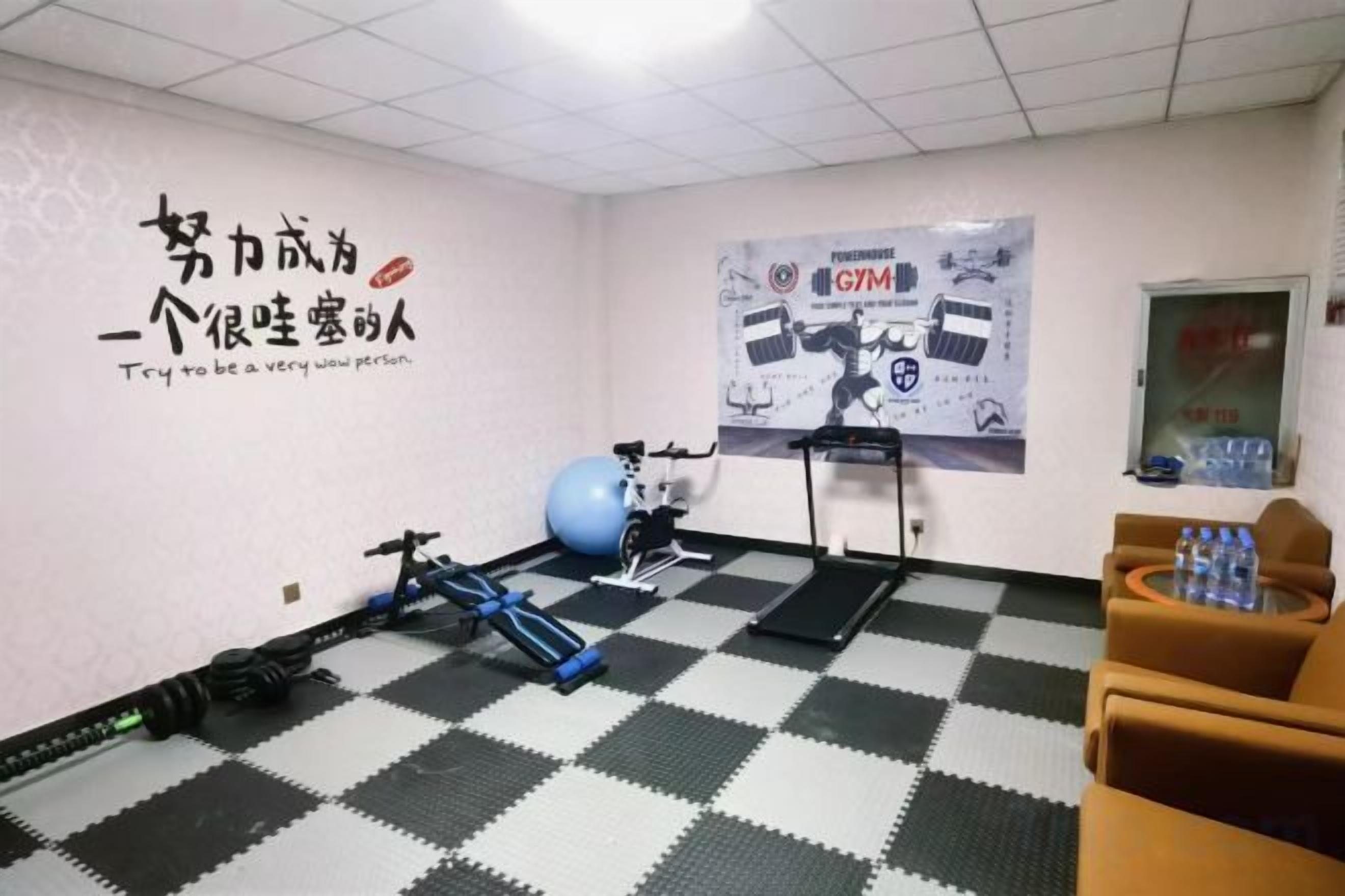 Un gimnasio con equipo de ejercicio, piso a cuadros blanco y negro, un cartel en la pared y un dispensador de agua.