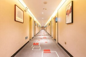 A hotel hallway with framed artwork on the walls, a carpet with geometric patterns, and doors leading to rooms. - Zhangye Xilaishun Holiday Hotel (Railway Station No.1 Middle School) (Zhangye)