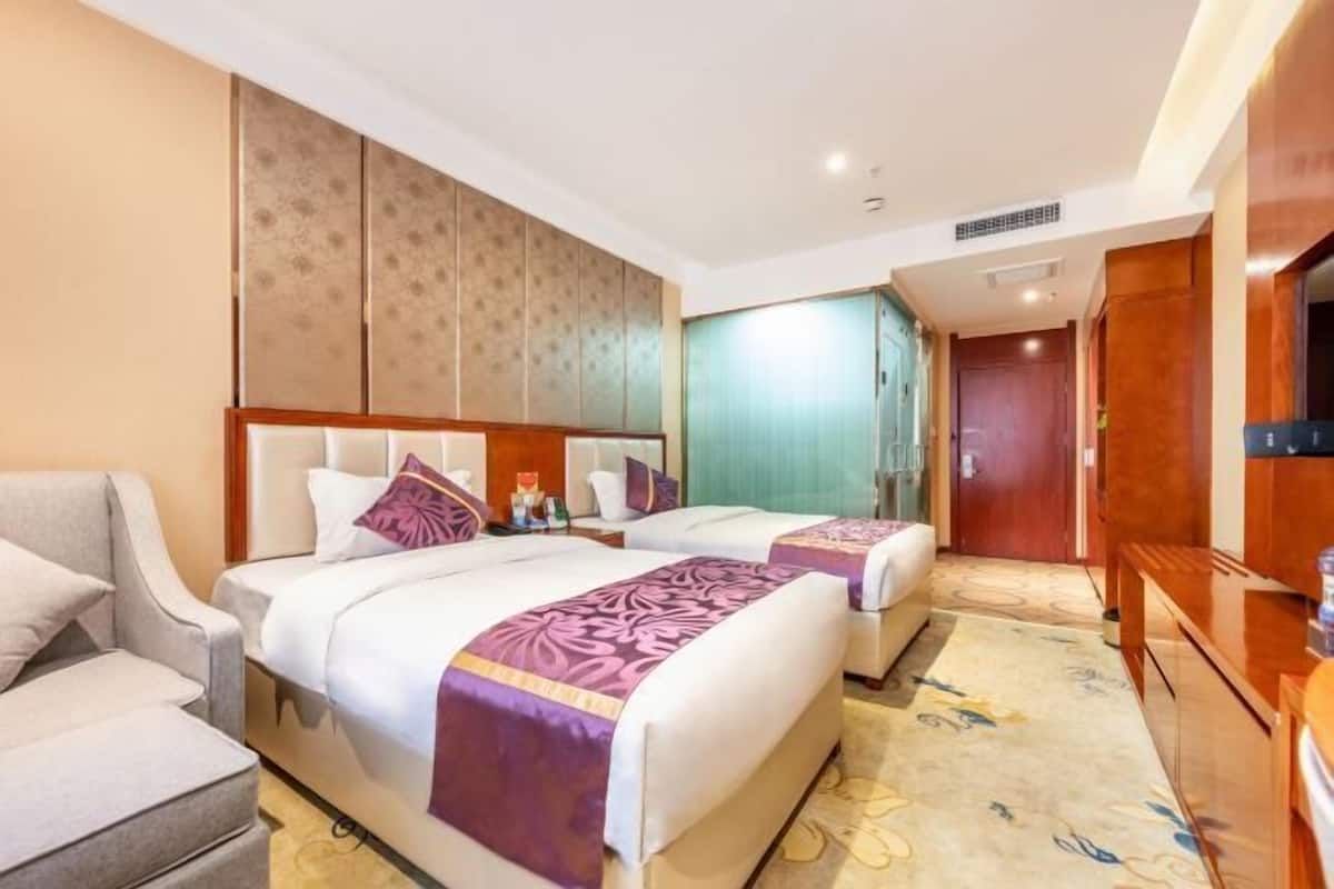 Een hotelkamer met twee bedden, een bank, een televisie en een zichtbare badkamer door een deur.