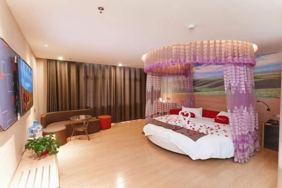 Een slaapkamer met een hemelbed, een bank, een kleine tafel en een aan de muur bevestigde televisie.