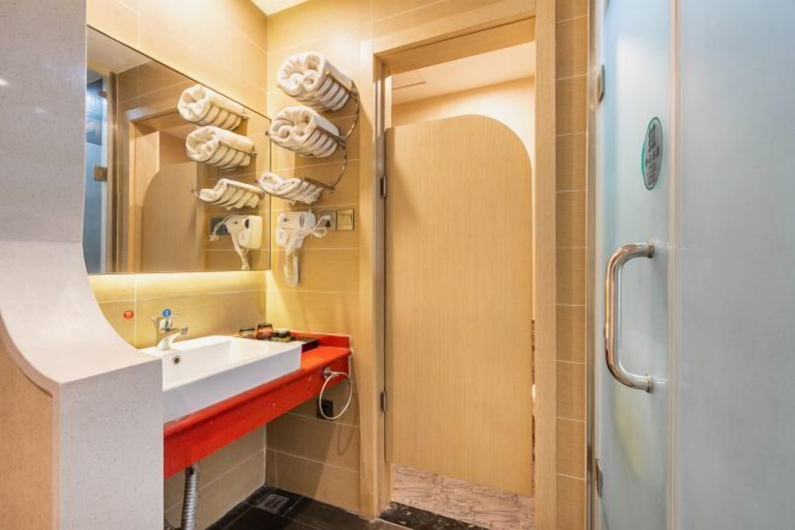 A bathroom with a white sink, red countertop, and a mirror. There are towels hanging on a rack and a shower door.