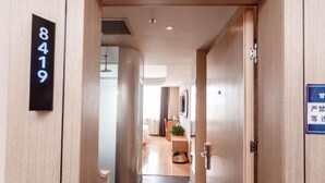 Ein Hotelkorridor mit einer Nummernschild und einem blauen Schild mit japanischen Schriftzeichen, sowie ein Blick in einen Raum mit Bett und Pflanze.