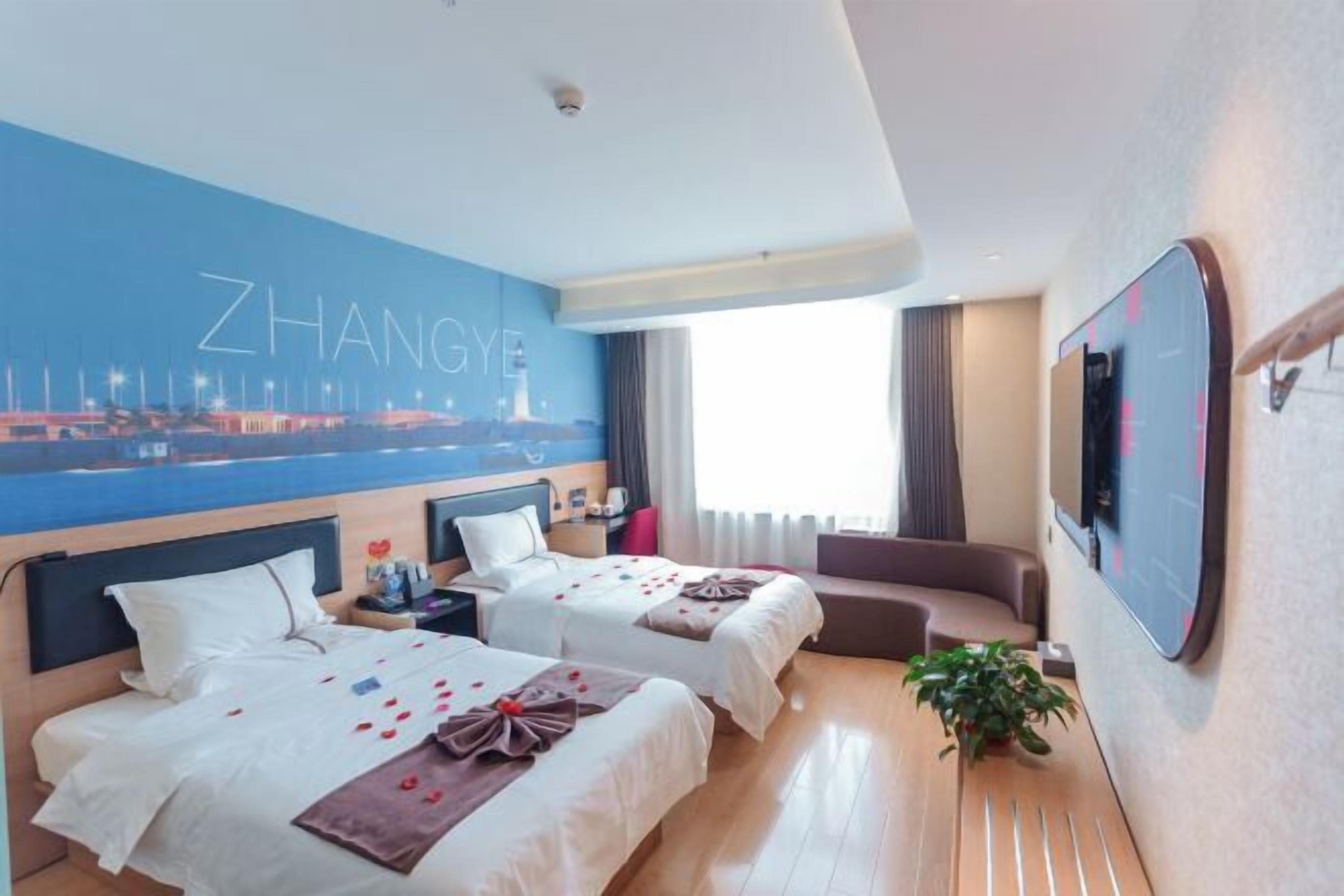 A hotel room with two beds, a large wall mural, a TV, and a plant.