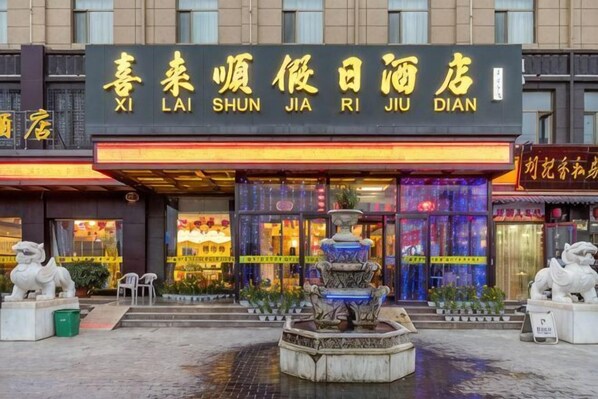 L’entrée d’un hôtel, avec une enseigne en caractères chinois, une fontaine et deux statues de lions en pierre.