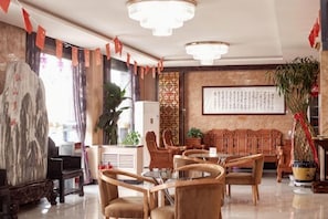 Un hall d’hôtel avec un canapé en bois de style traditionnel, une table ronde et une grande plante en pot.