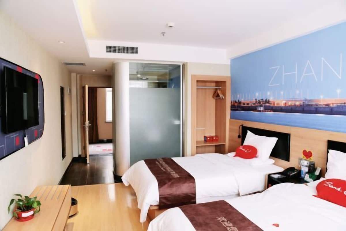 Hotelkamer met twee bedden, een televisie, een bureau en een groot raam met uitzicht op de stad.