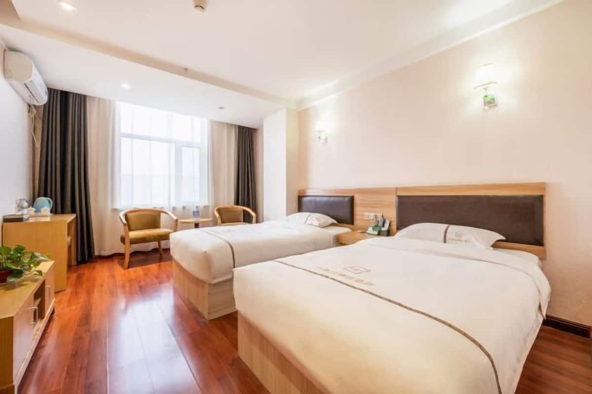 Een hotelkamer met twee bedden, een bureau met stoel, een televisie en een raam met gordijnen.