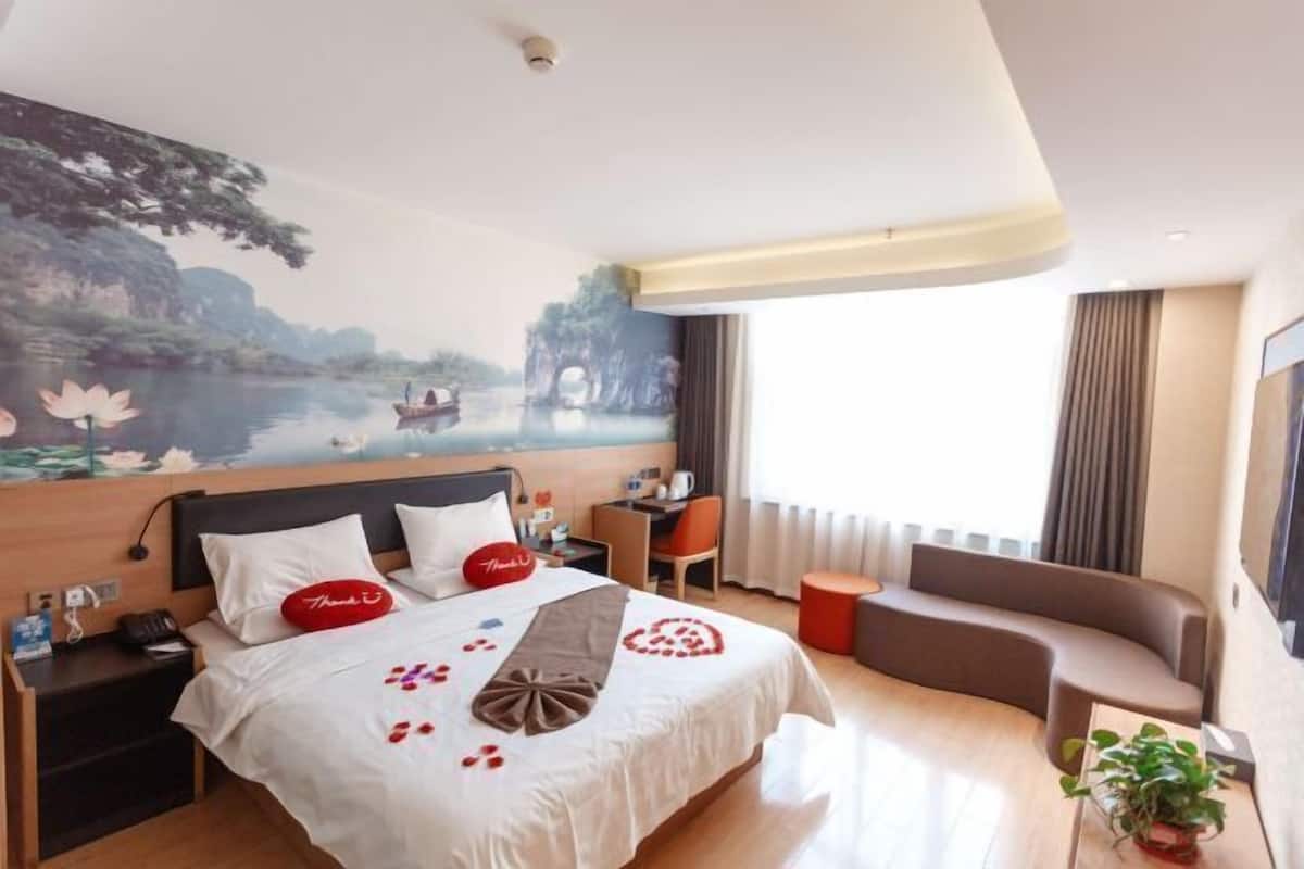 Een hotelkamer met een bed, een bureau, een stoel, een bank, een nachtkastje en een muurschildering.