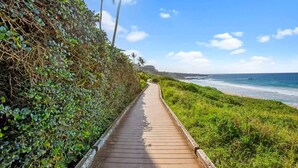 Un paseo marítimo de madera que conduce a una playa con abundante vegetación y palmeras.