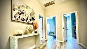 Un couloir doté d’un plancher en bois, d’une console blanche et d’un grand tableau abstrait.