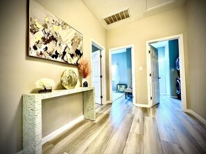 Un couloir doté d’un plancher en bois, d’une console blanche et d’un grand tableau abstrait.