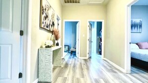 Un couloir doté d’un plancher en bois, d’un luminaire au plafond et de portes donnant sur d’autres pièces.