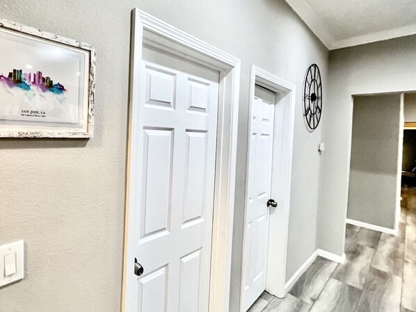 A hallway with two white doors, a framed cityscape picture, and a wall clock.