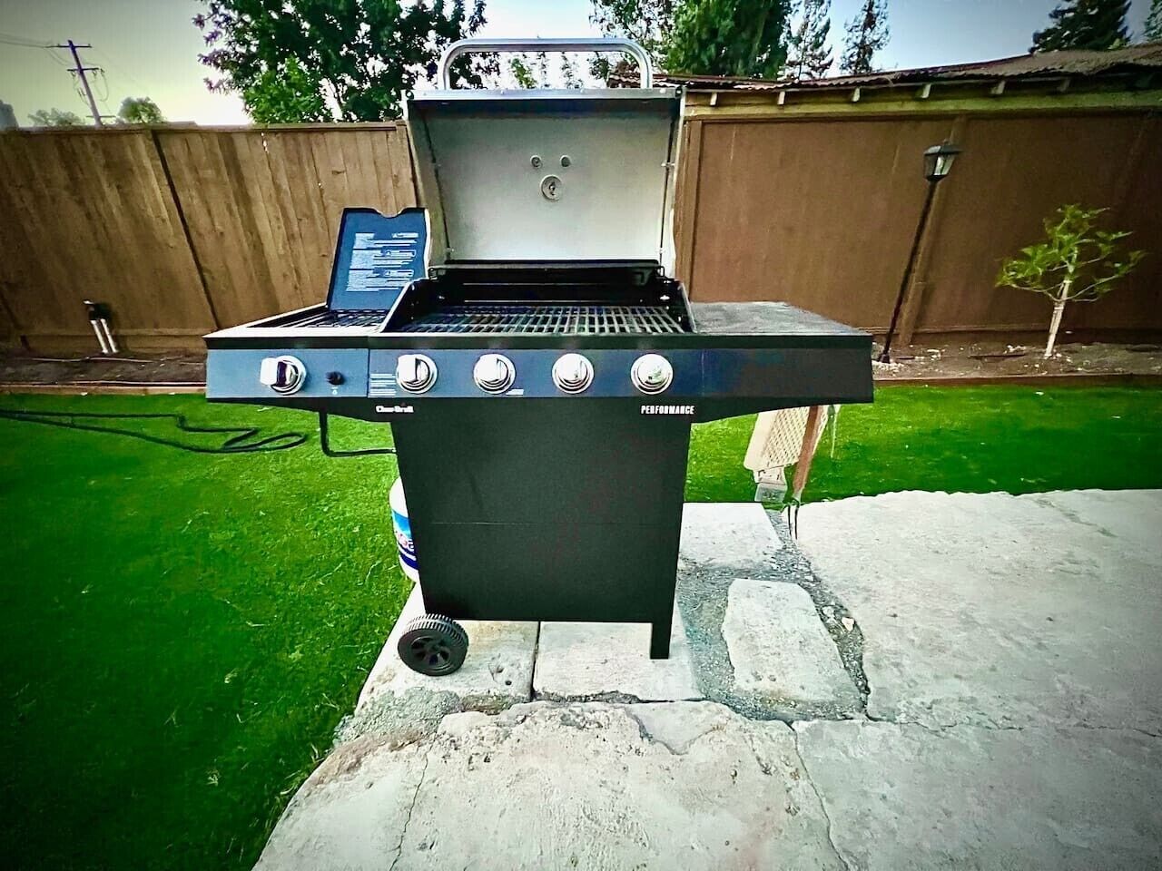A portable grill with a digital display, four control knobs, and a gas tank.