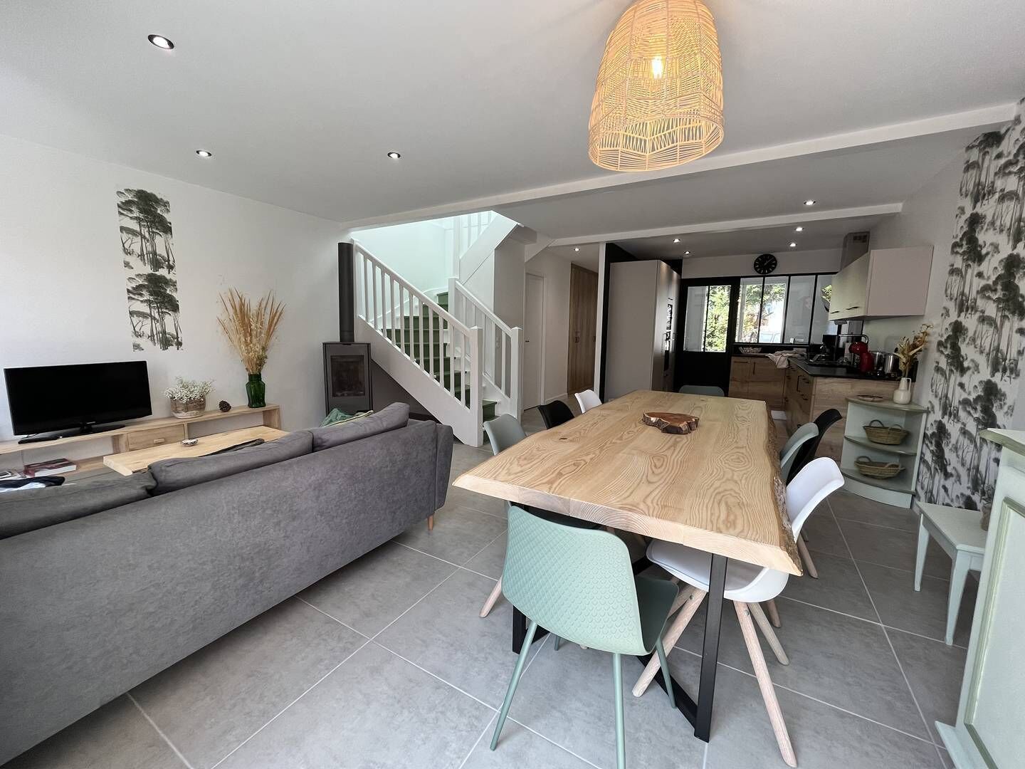 A modern living space with a sofa, dining table, chairs, a television, and a staircase.