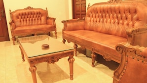Een kamer met een grote leren bank, een bijpassende fauteuil en een glazen salontafel.