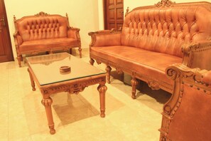 Een kamer met een grote leren bank, een bijpassende fauteuil en een glazen salontafel.