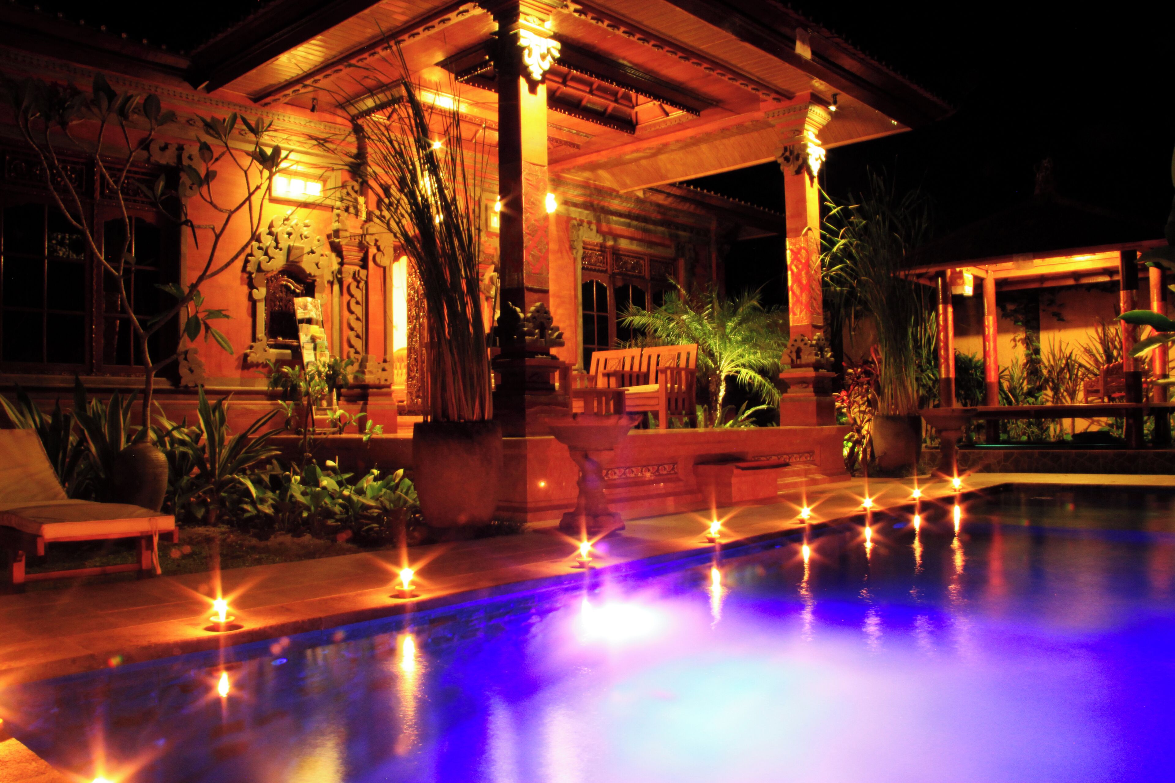 A poolside area with a covered seating area, lounge chairs, and a water feature with lights.
