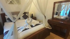 Ein Bett mit weißen Bettwäsche und einem Baldachin, ein Nachttisch mit Lampe und ein Spiegel an der Wand.