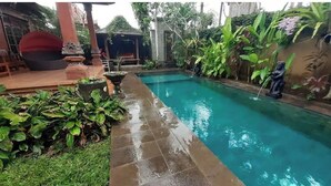 Ein rechteckiger Pool mit einer gefliesten Kante, umgeben von üppiger Vegetation und einem Kiesweg.