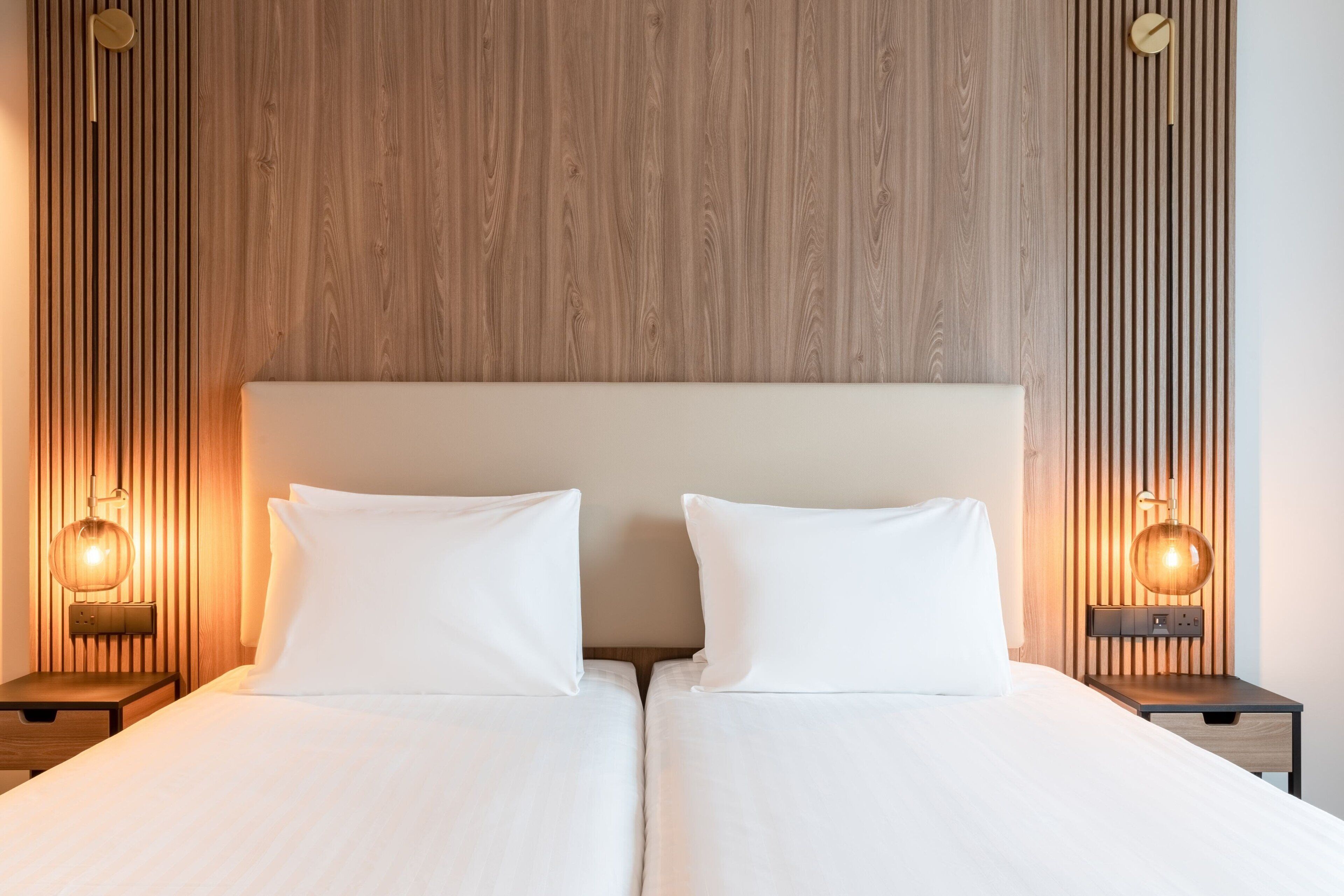 A double bed with white linens, two bedside tables with lamps, and a wooden slatted headboard.