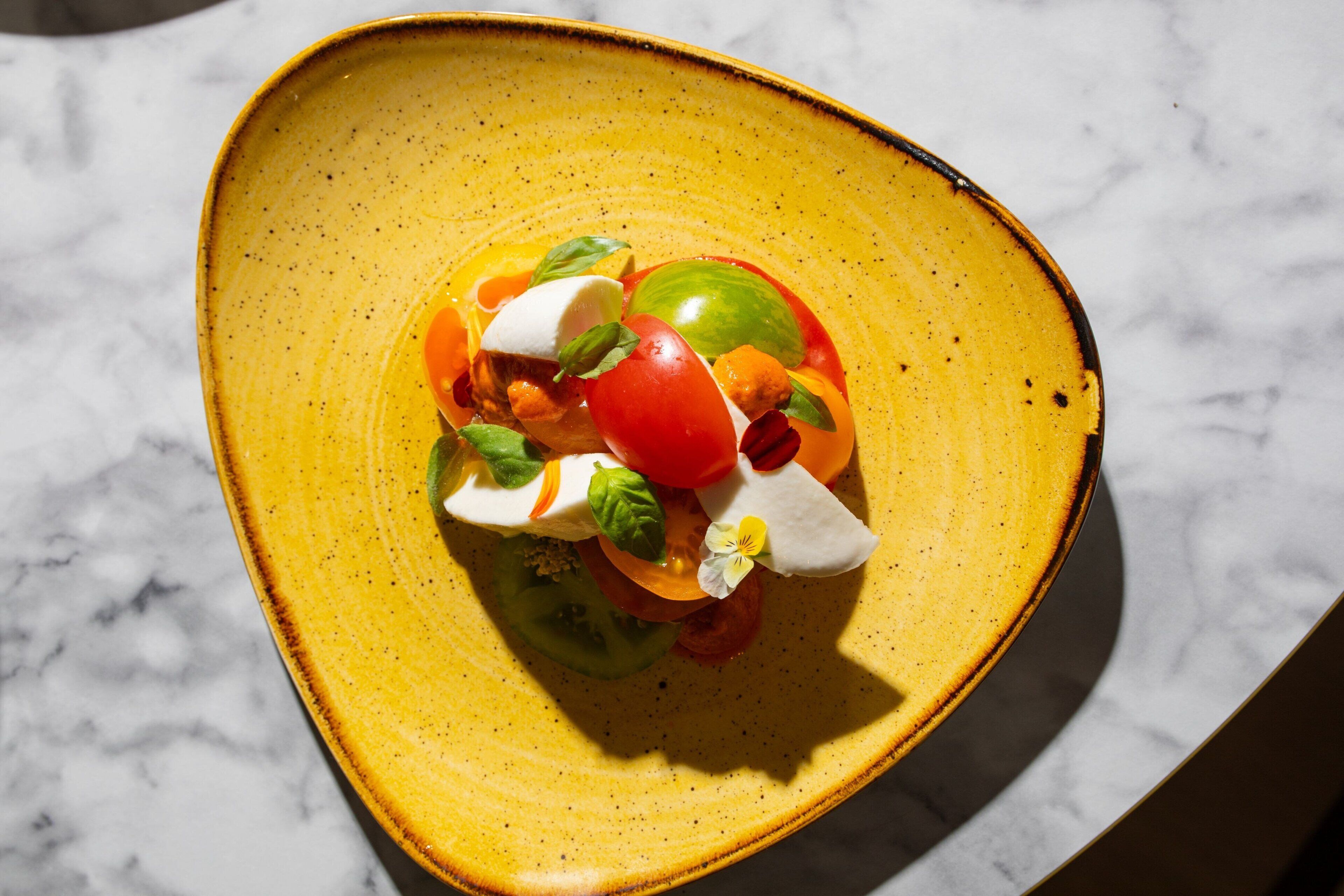 A yellow ceramic plate with a colorful salad on a marble surface.
