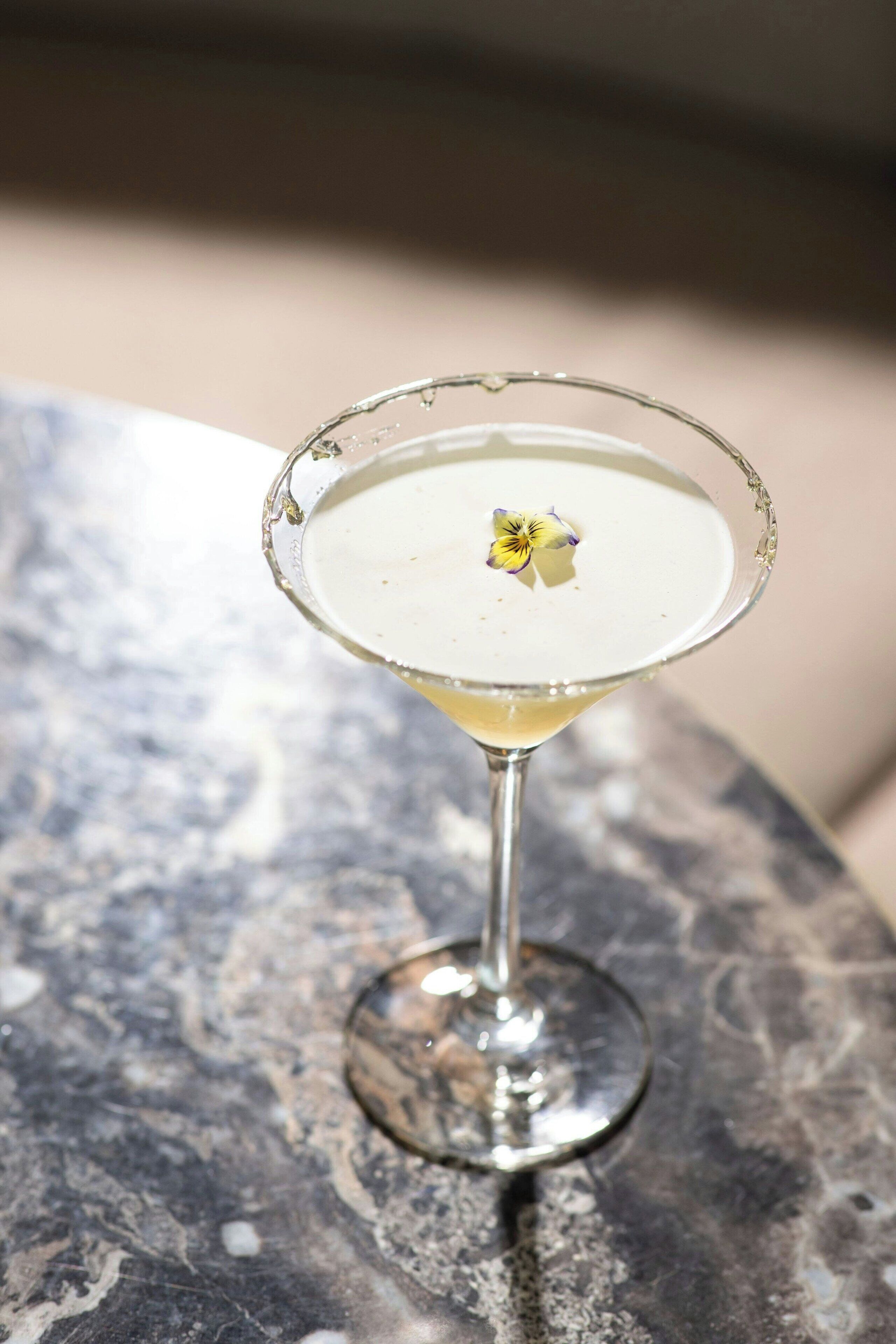 A martini glass with a flower garnish on a marble surface.