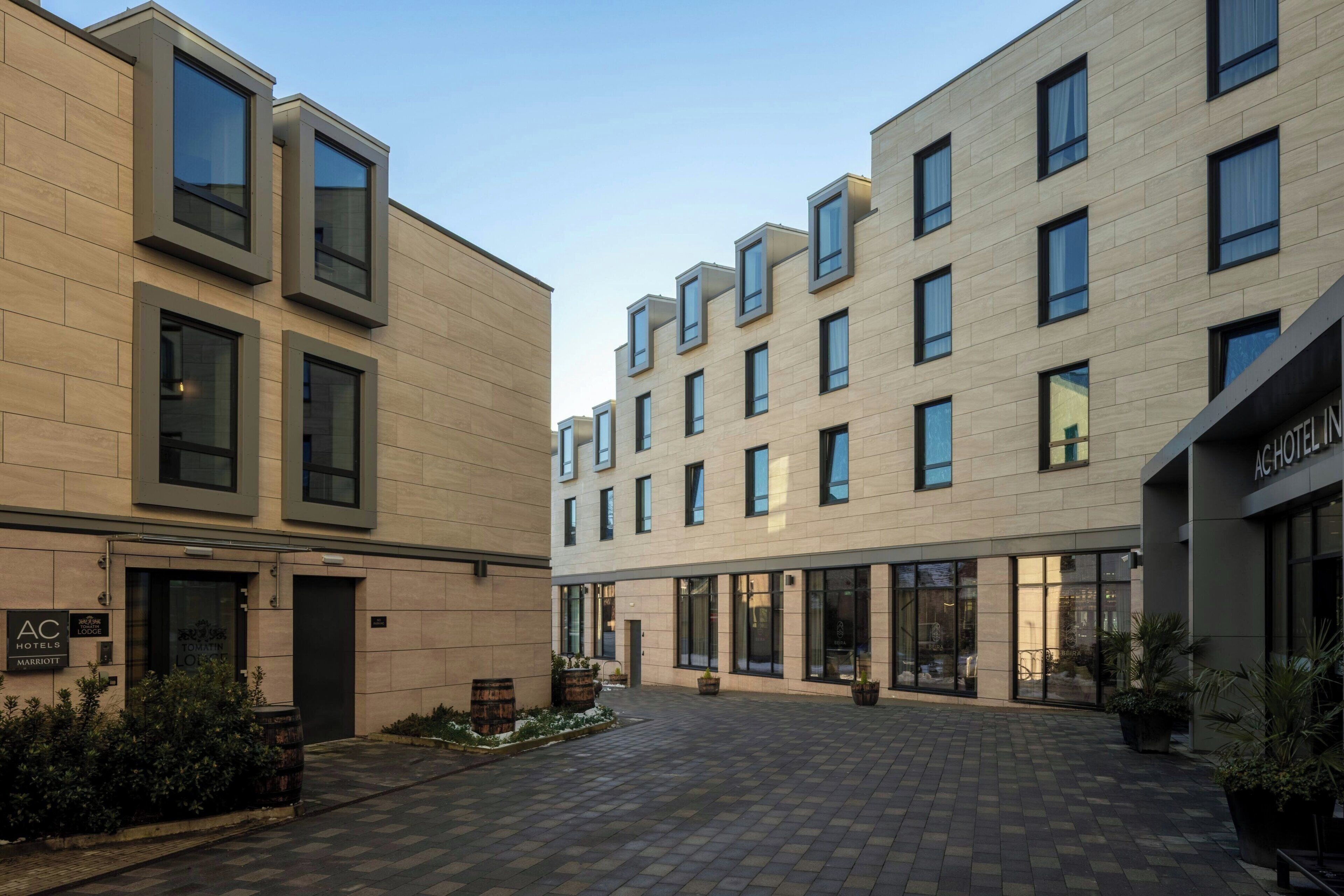 A modern hotel with a courtyard, featuring a mix of rectangular and square windows, a flat roof, and a clean, contemporary design.